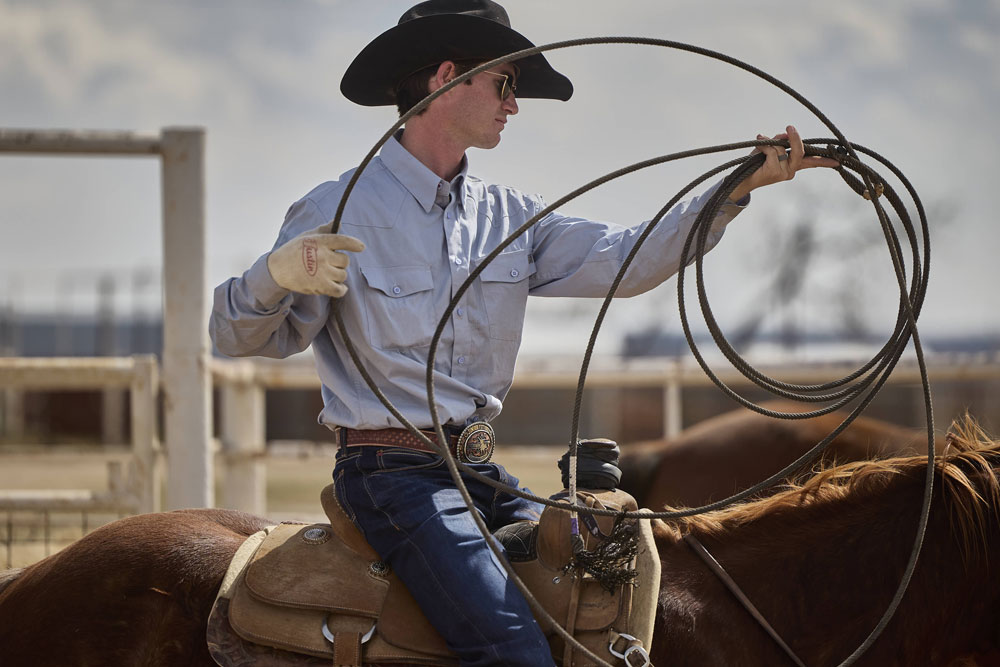 A cowboy holding a lasso while wearing a black cowboy hat.